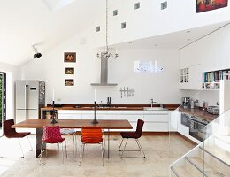 Minimalistischer Tisch mit Holzplatte und Stühle mit verschiedenen Bezügen in offener Designerküche