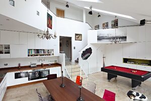 Blick über Essplatz und Einbauküche auf Billardtisch in nach oben offenem Raum mit umlaufender Galerie