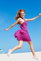 A happy young woman on a beach wearing a pink summer dress