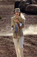 A blonde woman wearing a hat, a sand-coloured blazer, a blue blouse and beige trousers