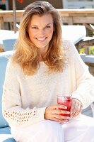 A young woman wearing a white knitted, open-work jumper holding a glass of lemonade