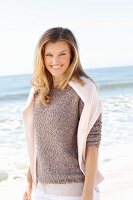A young woman on a beach with a jumper over her shoulders