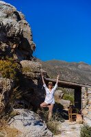 Frau bei Yogaübung an rustikalem Steinhaus über Meeresbucht