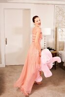 A young woman in a hotel room wearing an evening gown and holding a pink plush elephant