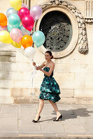 A young woman wearing a cocktail dress holding a bunch of balloons