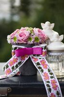 Romantic flower arrangement with embroidered ribbon next to glass vessel and cherubs on vintage case