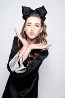 Young woman wearing dress with lace collar and large bow in hair blowing a kiss