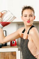 Junge Frau in Top und Latzhose trinkt roten Smoothie aus Mixer