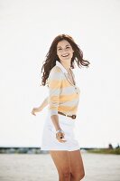 A brunette woman by a body of water wearing a long-sleeved T-shirt and a pair of shorts