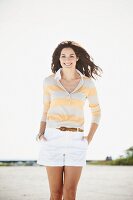 A brunette woman by a body of water wearing a long-sleeved T-shirt and a pair of shorts