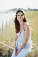 A dark haired woman wearing white trousers and a ruffled vest top