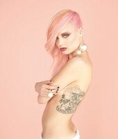 Junge Frau mit pastellrosa Haaren und großem Tattoo