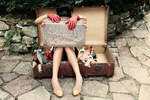 A woman with a suitcase on her knees sitting in a suitcase full of shoes