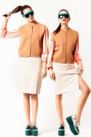 Two young woman wearing matching blouses, gilets, pencil skirts and platform shoes