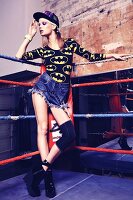 Junge Frau in Denim-Shorts und Batman-Shirt steht in Boxring