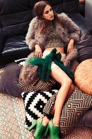 A young woman wearing shorts, a knitted top and a fur gilet lying on sofa cushions