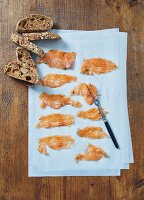 Homemade cured salmon on a piece of paper with slices of bread (seen from above)