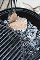 A smoked mixture being placed on glowing coals in a charcoal barbecue