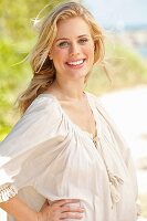 A young blonde woman on a beach wearing a white blouse