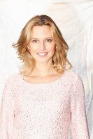 A blonde woman wearing a pastel pink jumper with Lurex and sequins