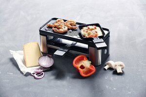 Raclettegerät für zwei Pfännchen mit Grillfläche, rundherum Zutaten für Raclette