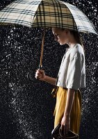 Young woman wearing white blouse and yellow skirt under black and yellow tartan umbrella