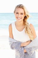 Junge blonde Frau in weißem Top und lila Strickjacke am Strand