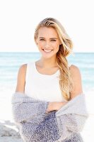 Junge blonde Frau in weißem Top und lila Strickjacke am Strand