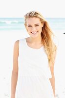 Junge blonde Frau in weißem Kleid am Strand