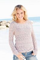 A young blonde woman by the sea wearing a knitted jumper and jeans