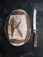 A whole loaf of sourdough rye bread next will bread knife (seen from above)