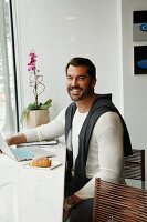 A man standing by a table with a laptop, coffee and pastries