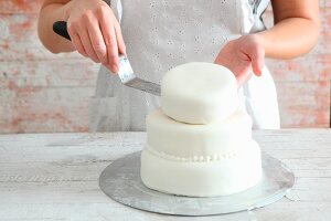 A multi-tier cake being decorated with white fondant icing
