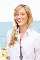 A young blonde woman by the sea wearing a white blouse and jeans