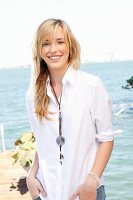 A young blonde woman by the sea wearing a white blouse and jeans