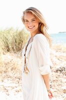 A young blonde woman on a beach wearing a white tunic