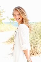 A young blonde woman on a beach wearing a white tunic