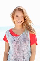 A blonde woman on a beach wearing a red top and a crocheted top