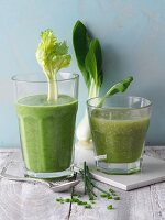 Two green smoothies garnished with celery sticks and bok choy