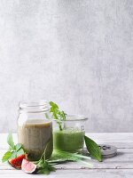Two green smoothies garnished with figs and herbs