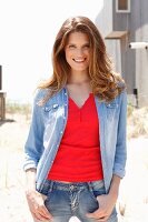 A young brunette woman wearing jeans, a red top and a denim blouse