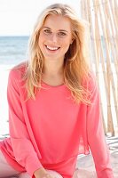 A young blonde woman sitting on a beach wearing a long-sleeved, layer-look top