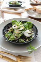 A place setting with a spinach and radish salad and miso dressing on a black plate