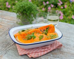 Quartered butternut squash with oil and herbs in a baking dish