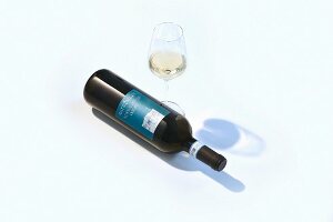 A glass of white wine and a bottle of wine lying on its side