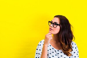 A thoughtful looking wearing glasses and a polka-dot t-shirt