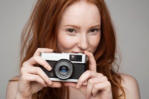 Junge rothaarige Frau hält Fotoapparat in den Händen