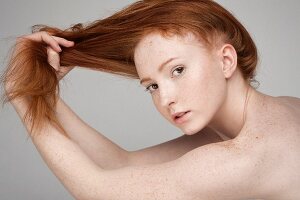 Portrait einer jungen rothaarigen Frau, die an ihren Haaren zieht