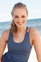 A young dark blonde woman on a beach wearing a purple tank top
