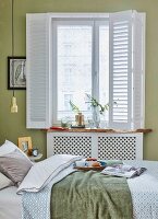 A breakfast table on a bed and in front of a window with a sliding white curtain in a green-painted bedroom